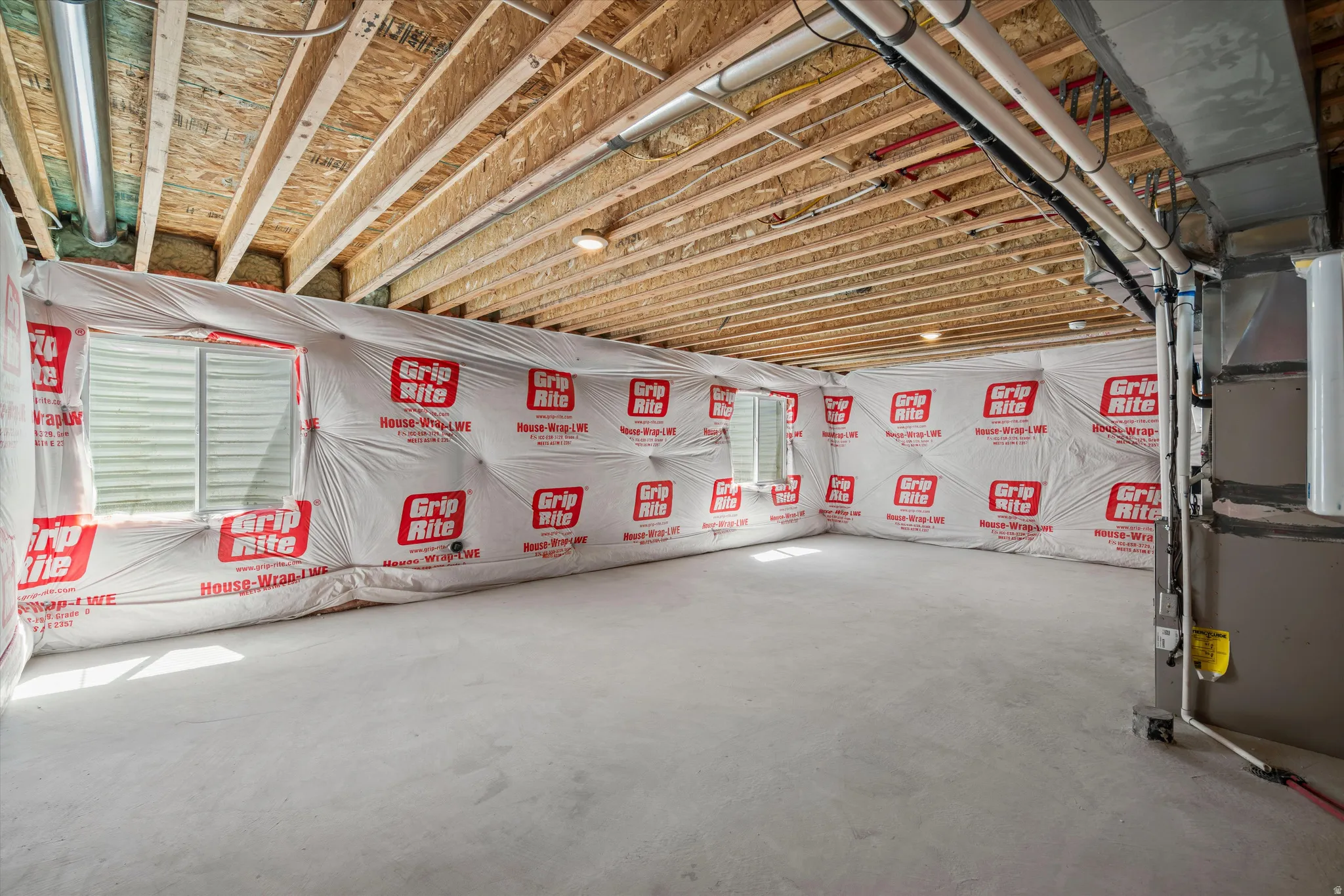 Unfinished basement with exposed wood joists, concrete flooring, and multiple window openings