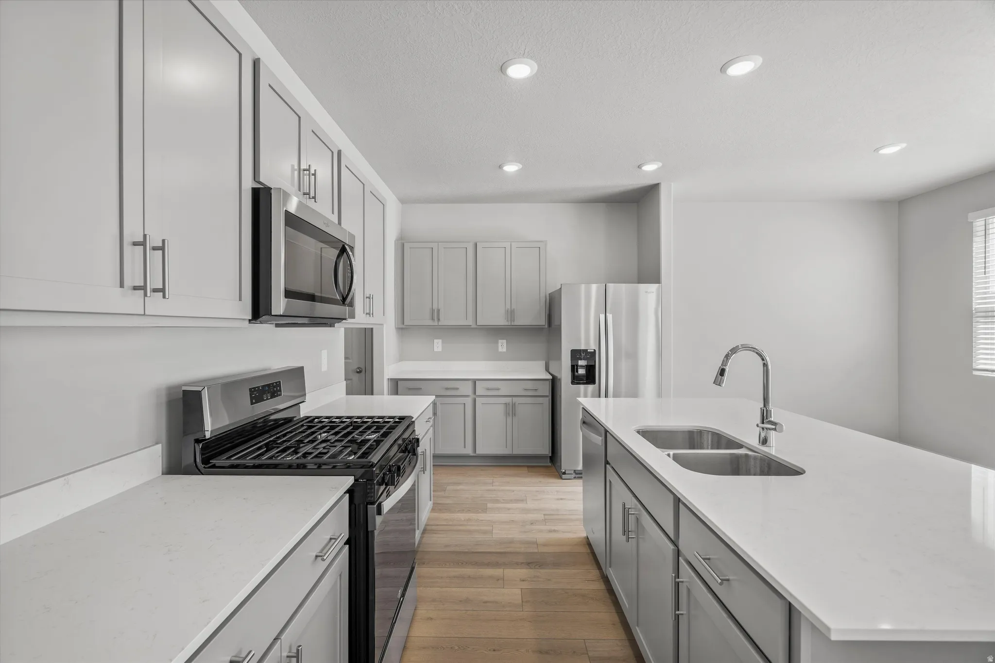 Kitchen featuring light wood-finish flooring, recessed lighting, stainless steel appliances, light gray cabinetry, and white countertops