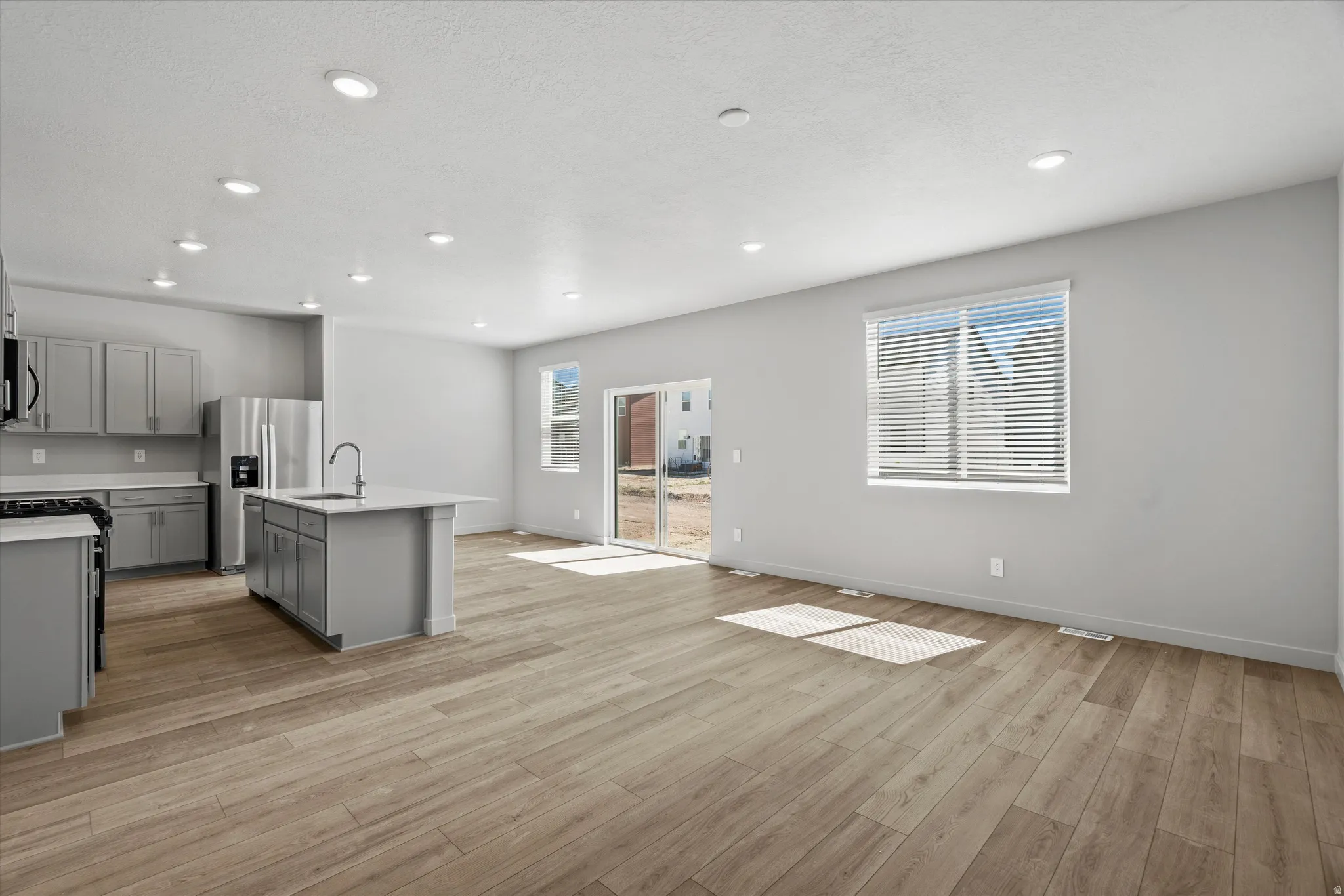 Open-concept living area with wood-finish flooring, recessed lighting, and a sliding glass door