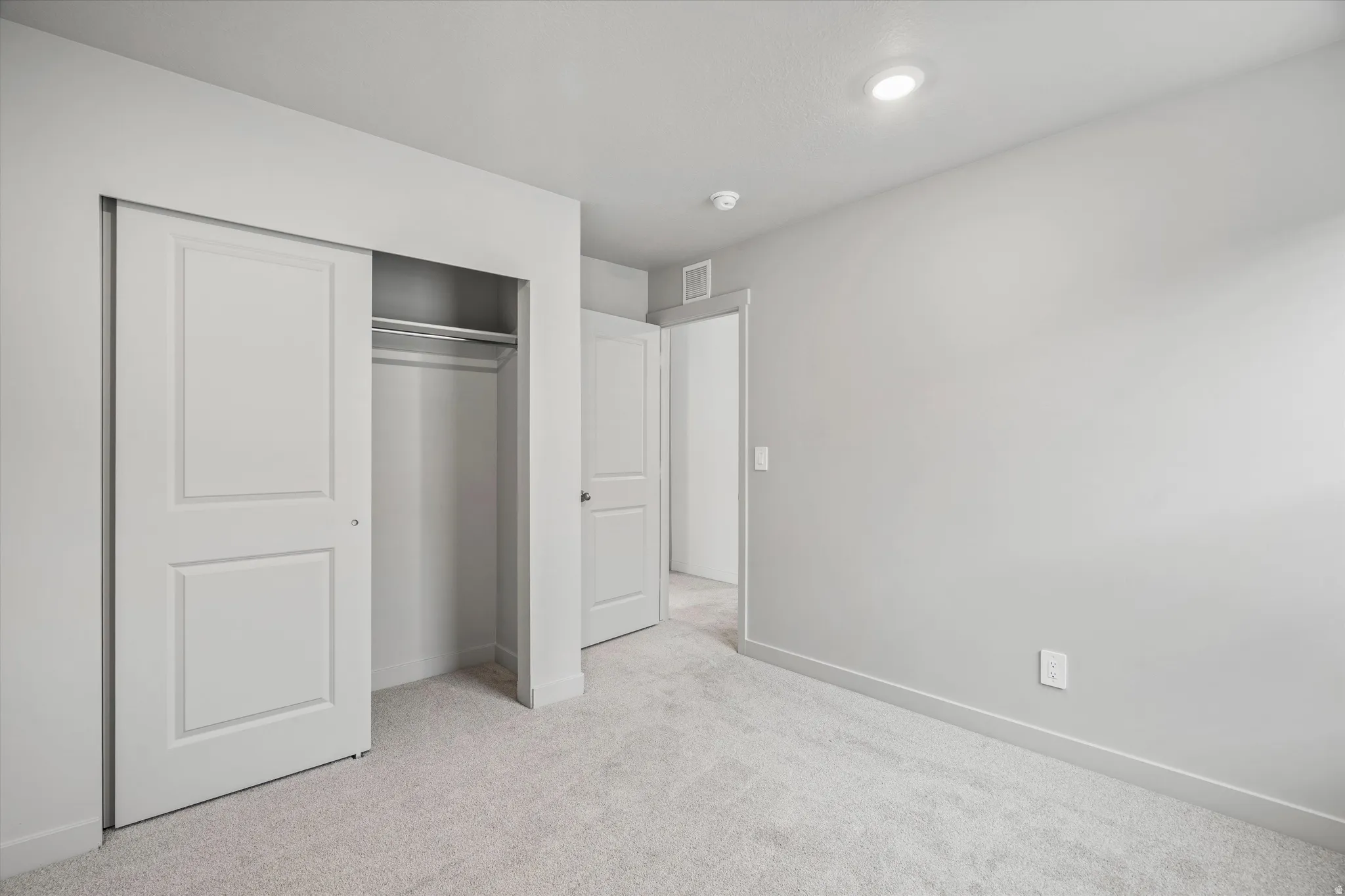 Neutral-toned wall paint, recessed ceiling lighting, light gray carpeting, and bi-fold closet doors with panel detailing