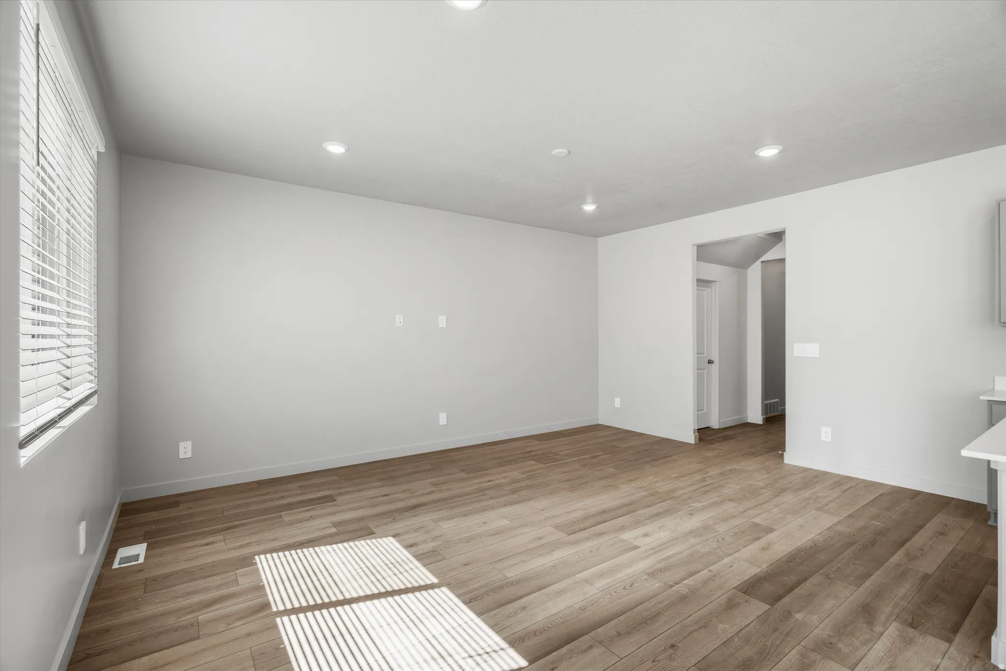 Spacious room featuring light wood-finish flooring, recessed lighting, and a window with horizontal blinds