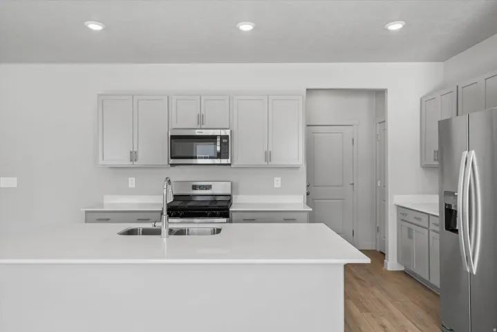 Kitchen featuring a large island with an undermount sink, stainless steel appliances, light-toned cabinetry, light countertops, and recessed lighting