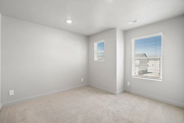 Plush carpet flooring, recessed ceiling lighting, two windows with blinds, and neutral wall tones
