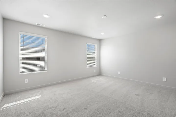 Neutral gray wall paint, recessed lighting, two windows with blinds, gray carpeting