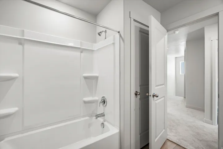 White bathtub with an integrated shower surround featuring chrome fixtures
