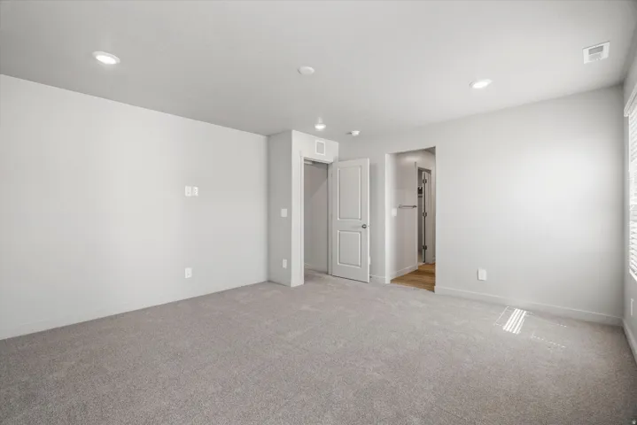 Spacious interior room with light gray carpeting, recessed ceiling lighting, and white walls