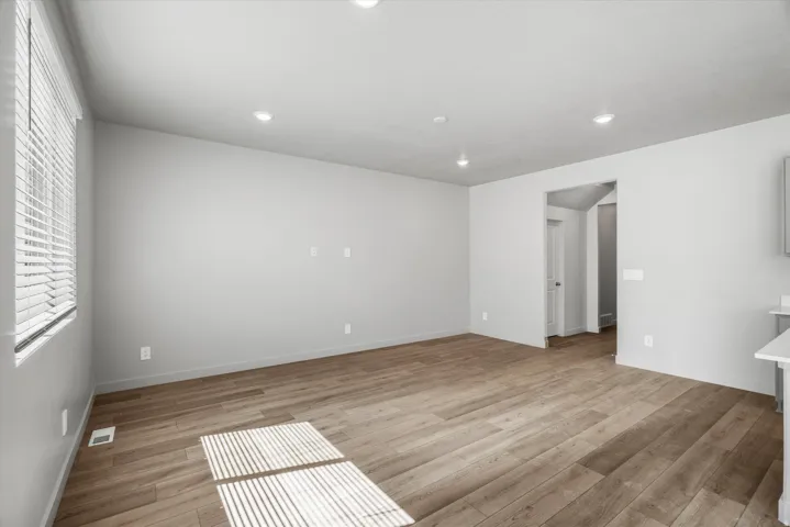 Spacious room featuring light wood-finish flooring, recessed lighting, and a window with horizontal blinds