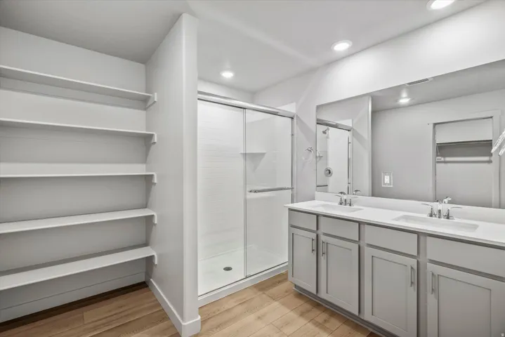 Spa-inspired primary bathroom featuring dual vanities with gray cabinetry, white quartz countertops, and chrome fixtures