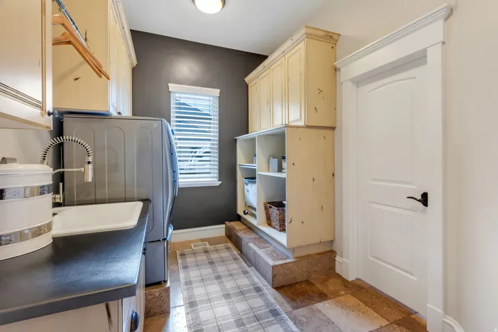 Built-in cabinetry, utility sink with a high-arc faucet, durable countertop, window with blinds, and tiled flooring.  There is plumbing and space for a second washer and dryer.