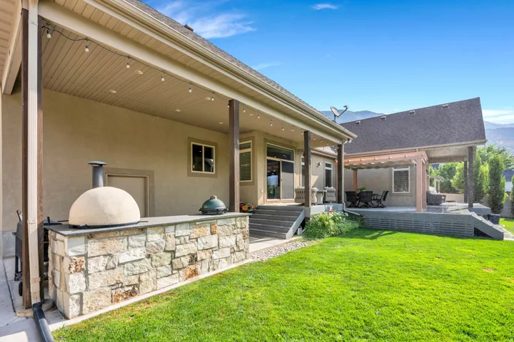 Expansive rear patio featuring a stone-clad outdoor kitchen, built-in pizza oven, covered outdoor dining area, and a pergola-covered section.
