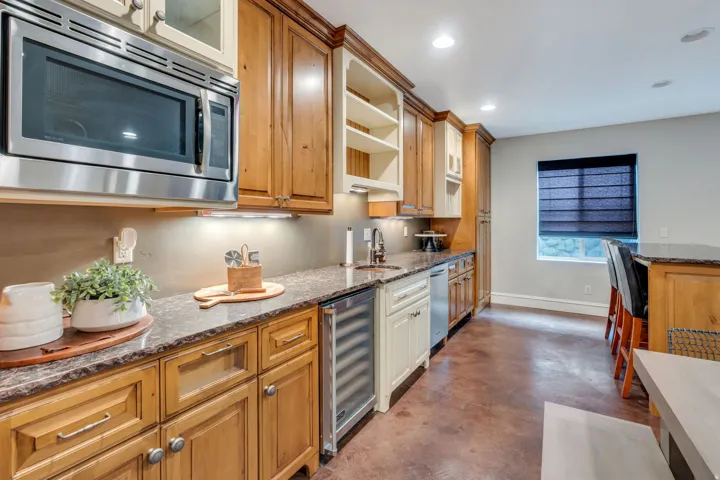 Integrated stainless steel microwave, stone countertops, under-cabinet lighting, wood-finish cabinetry, and an under-counter beverage cooler.