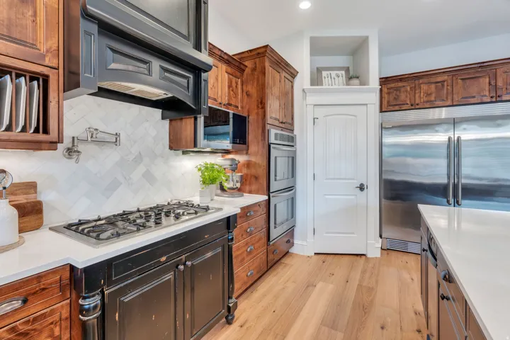 Gourmet kitchen featuring a gas range with pot filler, herringbone tile backsplash, double wall ovens, wood-finish flooring, and white countertops.