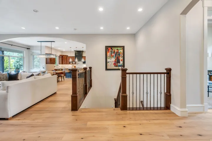 Light-toned wood-finish flooring throughout, recessed lighting, arched entryway, dark wood newel posts with iron balusters, and expansive windows.