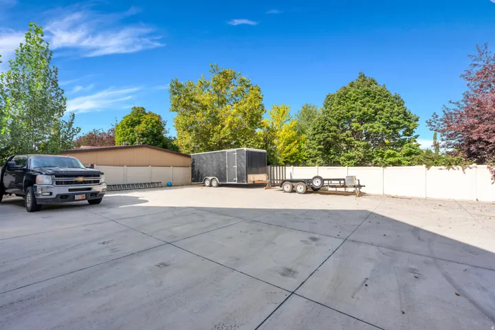 Expansive concrete paved lot with multiple outbuildings, including a metal storage structure and utility shed.