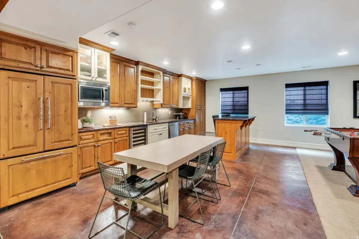 Second kitchen in basement. Full-height wood-paneled refrigeration, integrated microwave, wood cabinetry with glass-front accents, and a built-in beverage refrigerator.