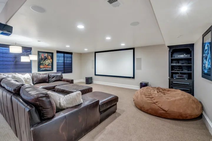 Integrated projection screen, built-in recessed lighting, in-ceiling speakers, wall-mounted projector, and a built-in media cabinet.