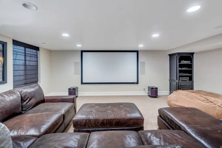 Dedicated media room featuring a large projection screen, recessed ceiling lighting, premium leather seating, and built-in cabinetry with shelving.