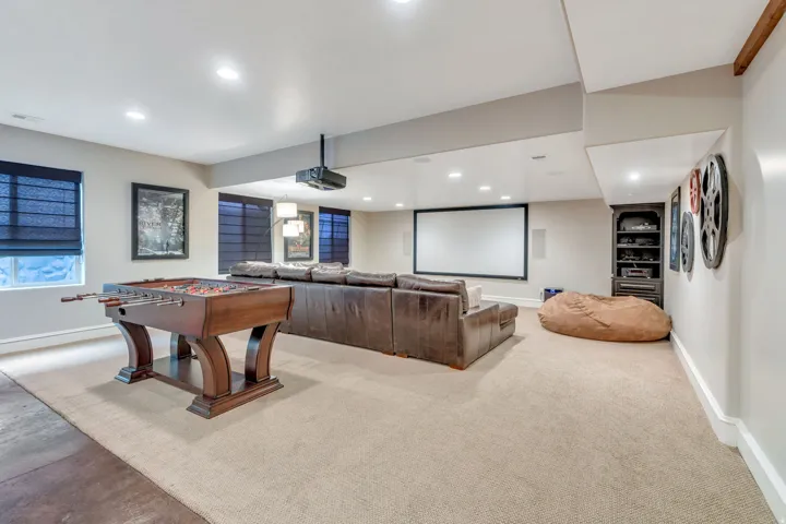 Expansive recreation room featuring engineered wood-finish flooring, recessed ceiling lighting, and a built-in wet bar with dark wood cabinetry.
