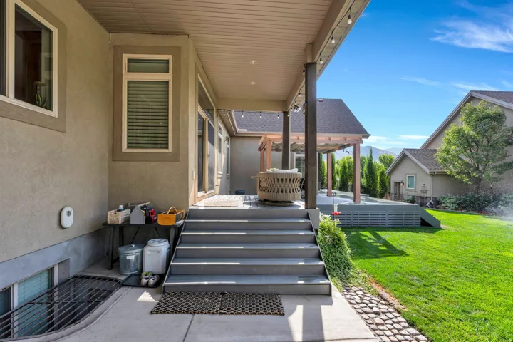 Covered rear patio featuring composite decking with integrated steps, aluminum pergola structure, and direct access to manicured lawn with mature landscaping.