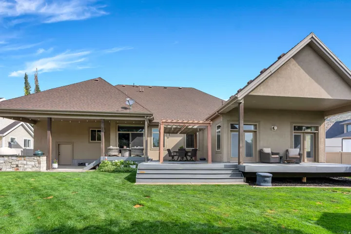 Expansive backyard featuring a manicured lawn, a large deck with multiple seating areas, a wood pergola, and a stone outdoor kitchen.