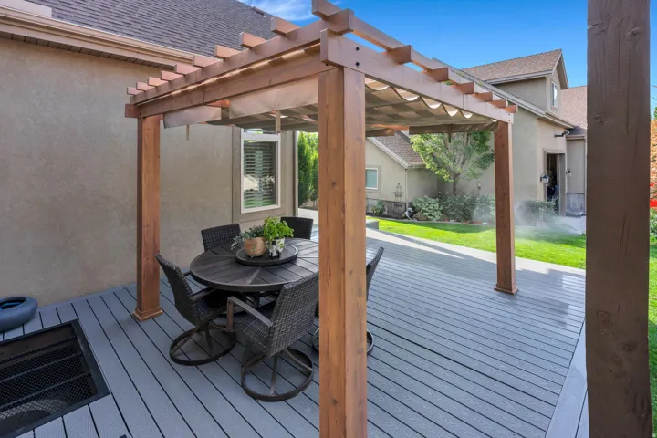 Expansive outdoor deck featuring a wooden pergola with a retractable canopy, a built-in access well, and a manicured lawn.