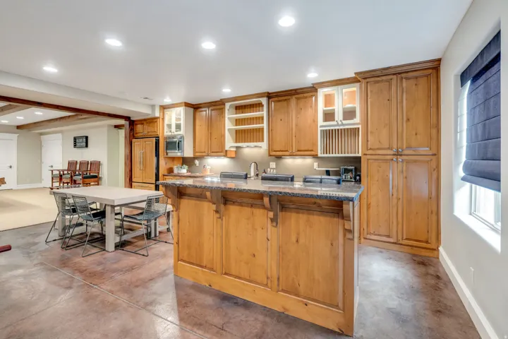 Spacious kitchen featuring warm wood cabinetry with glass-front upper storage, stainless steel appliances, a large center island with seating, and recessed ceiling lighting.