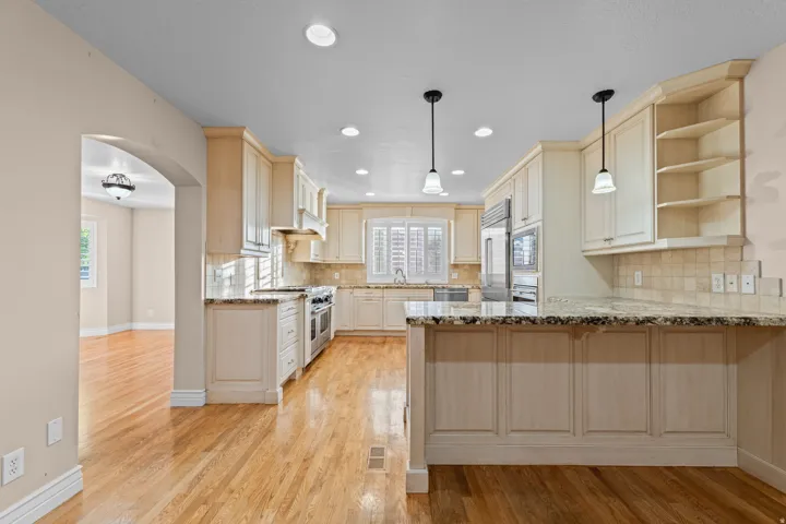 Kitchen featuring light-toned cabinetry, stainless steel appliances, recessed lighting, pendant lights, and wood-finish flooring