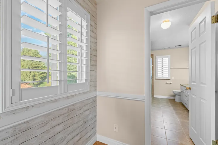 Window with white plantation shutters, wood-finish accent wall, and crown molding