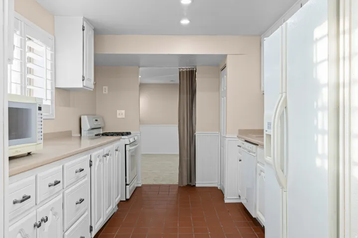 Kitchen with white cabinetry, light-toned countertops, tile flooring, and white appliances