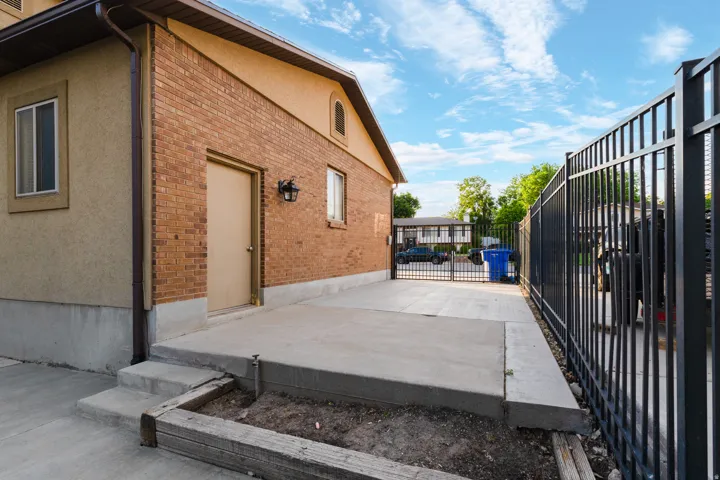 Brick and stucco exterior with multiple windows, concrete patio, concrete steps, and a black metal fence