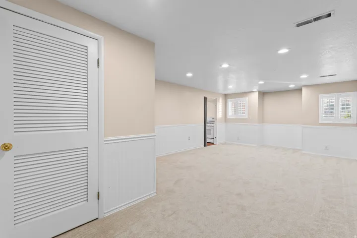 Spacious room featuring neutral carpeting, wainscoting, recessed lighting, and louvered windows