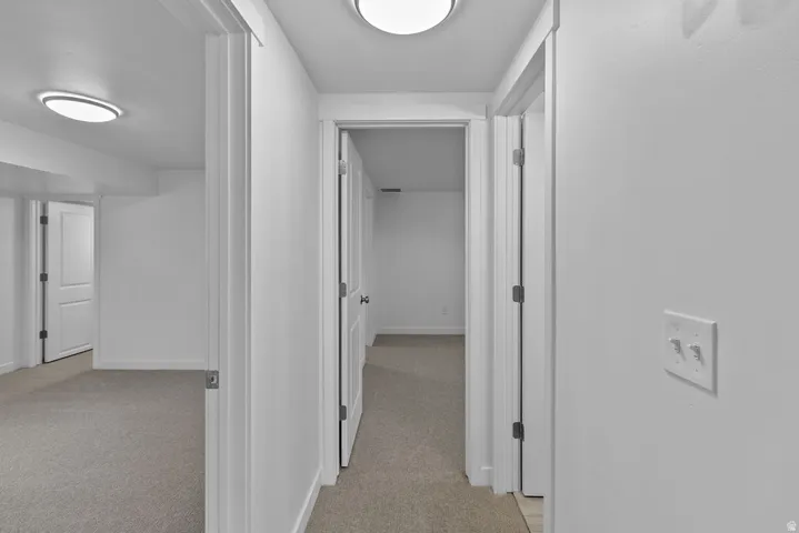 Carpeted hallway with flush-mount lighting, white walls, and multiple doorways