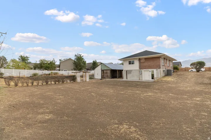 Expansive lot featuring a brick and siding exterior, a dark shingle roof, a white perimeter fence, and a detached shed structure