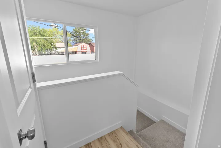 White interior walls, wood-finish flooring, carpeted stairs, and window with exterior exposure
