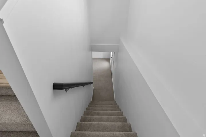 Carpeted staircase with a dark handrail, white painted walls, and overhead lighting