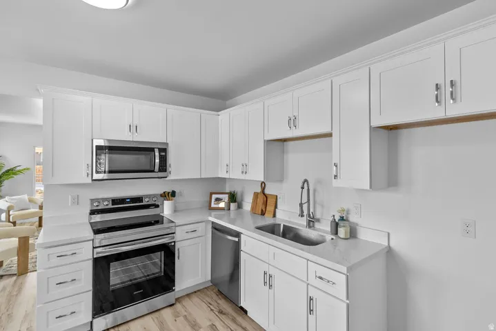 White cabinetry, stainless steel appliances, light-toned countertops, and wood-finish flooring