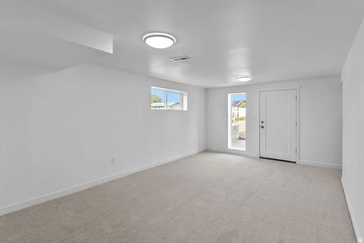 Recessed lighting, light gray carpeting, crisp white walls, white egress door, and a white-framed window