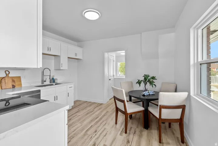 White cabinetry with brushed nickel hardware, light-toned wood-finish flooring, white countertop surfaces, and a stainless steel sink with a gooseneck faucet