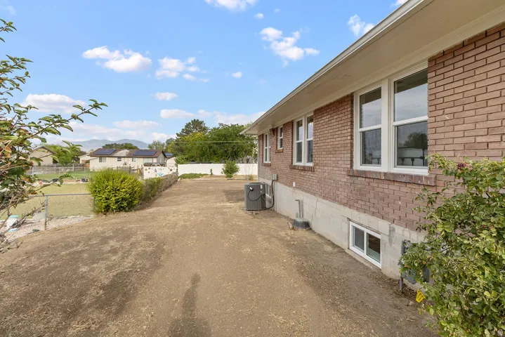 Brick exterior, multiple windows, compact air conditioning unit, established shrubbery, chain link fencing