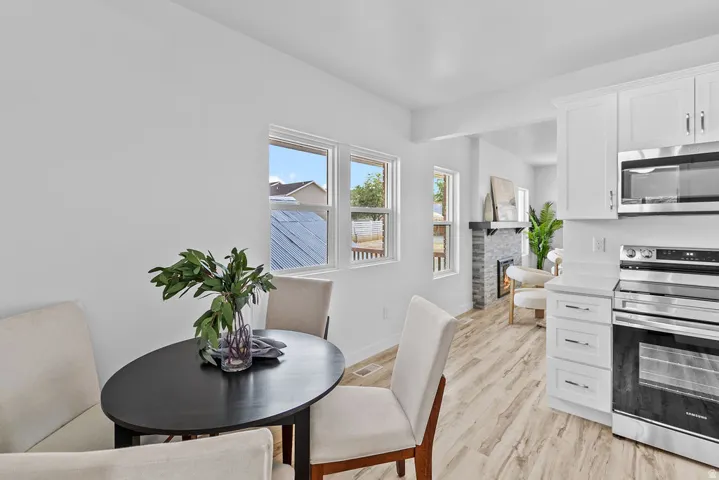 White shaker cabinetry, stainless steel appliances, stone fireplace with mantel, wood-finish flooring, and multiple windows