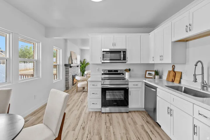 Kitchen featuring white cabinetry, stainless steel appliances, light-toned countertops, and wood-finish flooring