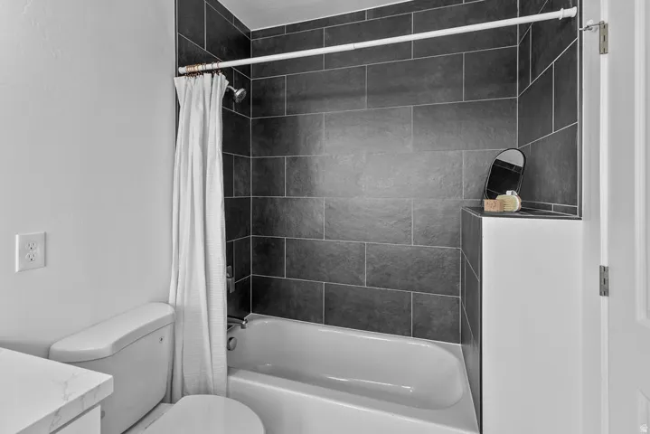 Bathtub with dark tile surround, white walls, and a built-in storage ledge