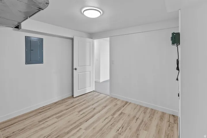 Wood-finish flooring with white baseboards, recessed ceiling lighting, and a paneled interior door