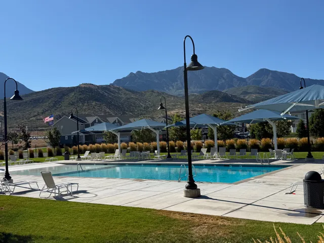 Community swimming pool with a surrounding concrete deck, multiple shade structures, and mountain scenery