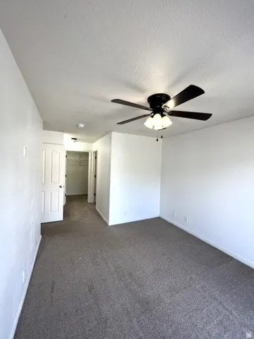 Neutral-toned carpeting, white walls, white paneled door, and a ceiling fan with integrated lighting