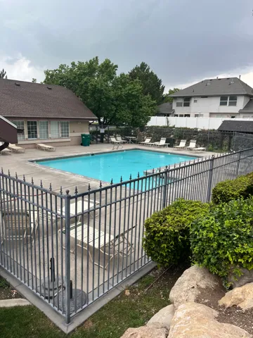 Outdoor swimming pool with surrounding concrete decking, secured by a wrought iron fence