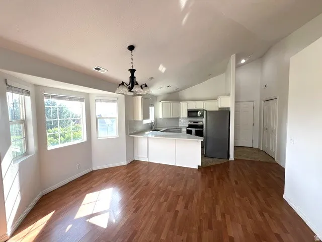 Open-concept living area featuring vaulted ceilings, wood-finish flooring, a kitchen island with seating, stainless steel appliances, and a bay window