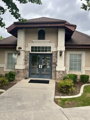 Stone facade entry with double glass doors, sconce lighting, and manicured landscaping