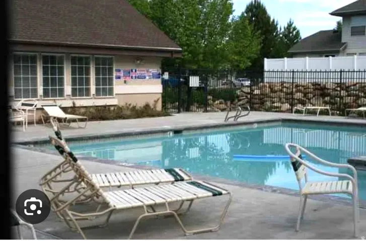 Outdoor swimming pool with concrete decking, surrounded by a black metal fence and a retaining wall with natural stone elements
