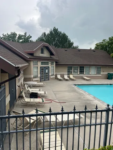 Resort-style backyard oasis featuring a sparkling in-ground swimming pool, expansive concrete patio with lounge seating areas, and a spacious poolside cabana with multiple French doors and arched architectural detailing